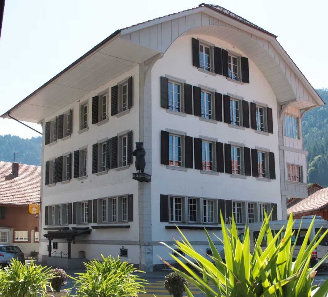 Das Gruppenhaus in Boltigen von aussen, weisser Altbau mit dunklen Fensterlaeden und Baerenfigur ueber dem Eingang