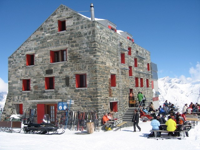 2003 Saas Fee - Saas Grund: Berghaus aus Naturstein mit roten Fensterläden, davor Gaeste auf der Sonnenterrasse