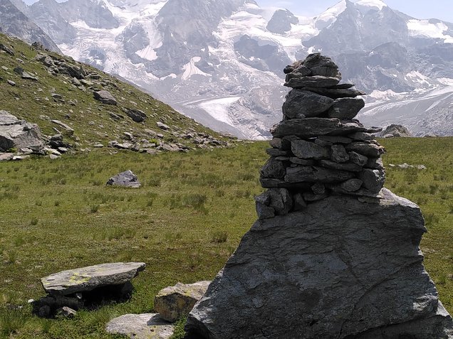 Steinmann aus geschichteten Platten auf einer Alpwiese vor einem Gletscher