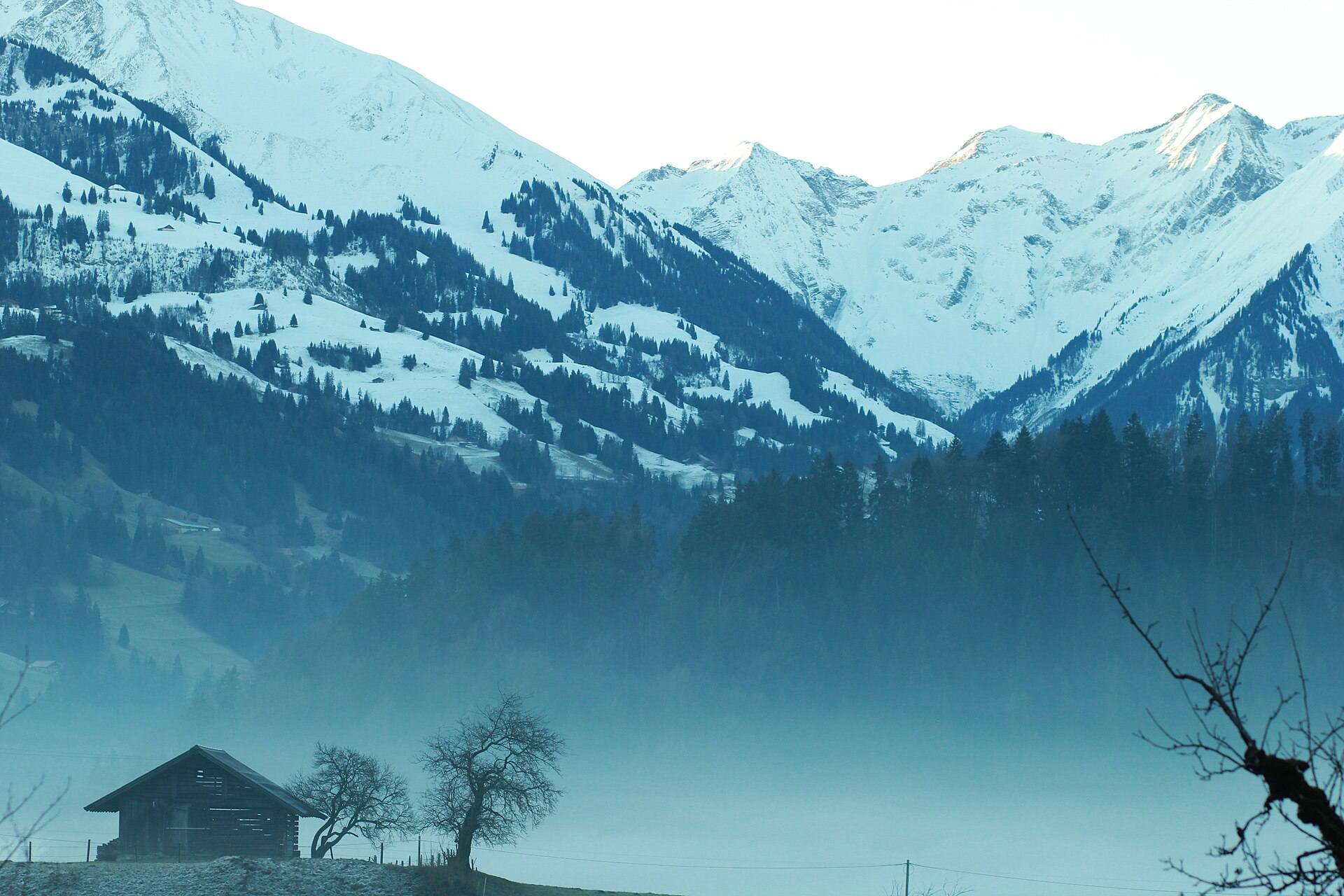 Weites Bergtal im Winter, ein einzelnes Bauernhaus am Hang